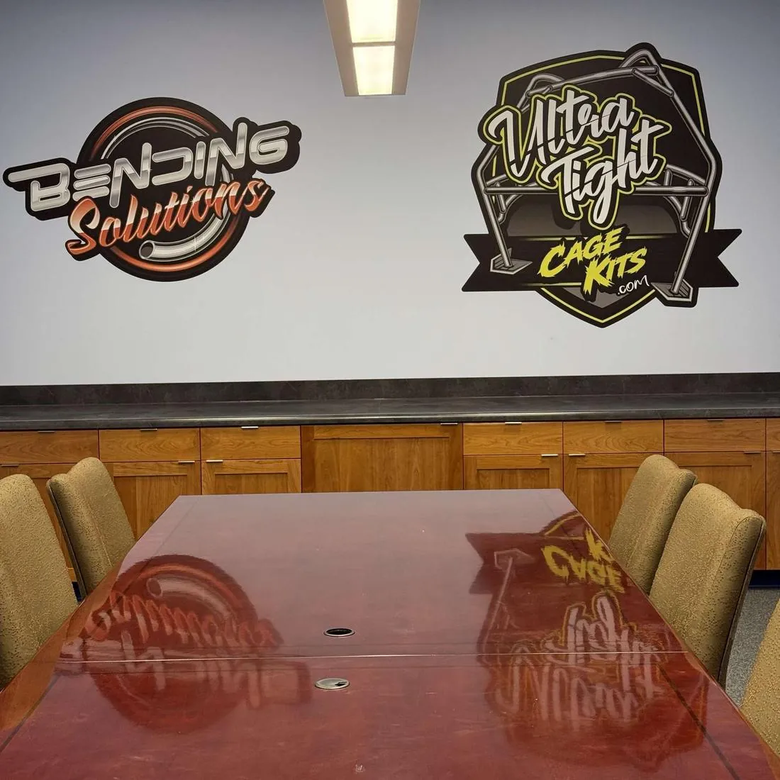 Bending Solutions and Ultra Tight Cage Kits logos printed on a conference room wall